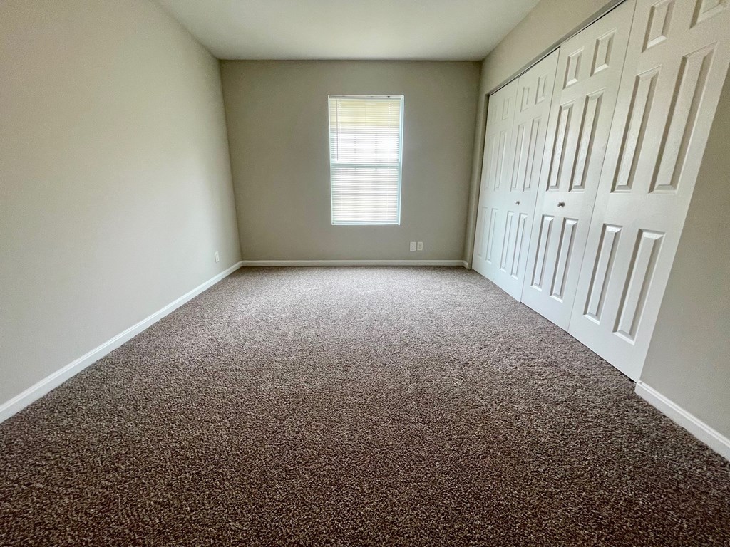 A room with a carpeted floor and a window with blinds.