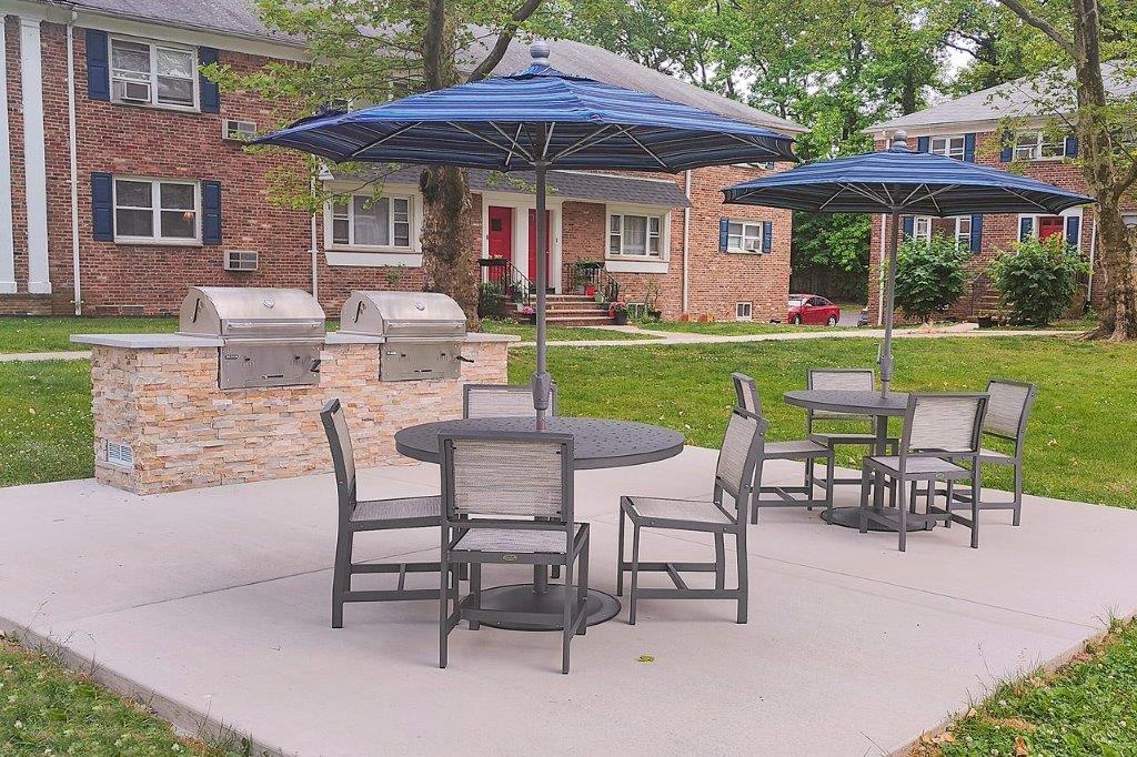 Two outdoor grilling stations next to two tables with chairs and umbrellas