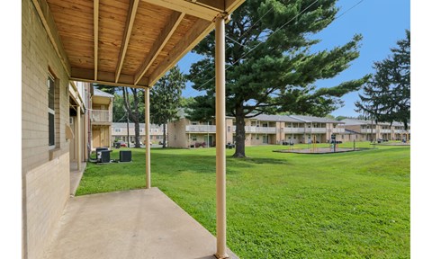 A view of a porch with a green lawn and trees in the background.