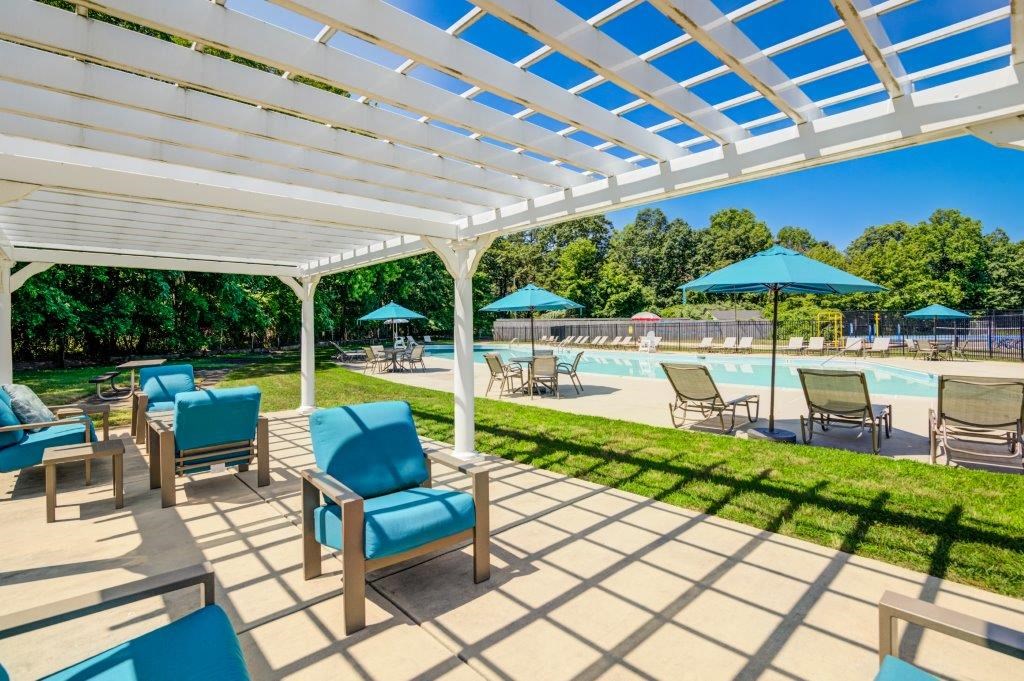 a covered patio with chairs and umbrellas near a swimming pool