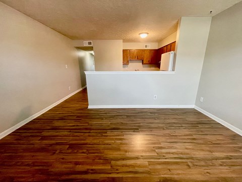 an empty living room with wood flooring and a kitchen