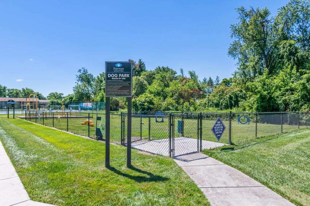 a dog park with a fence and a sign on a sidewalk