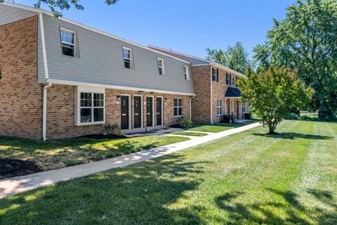 a brick apartment building with a sidewalk and grass