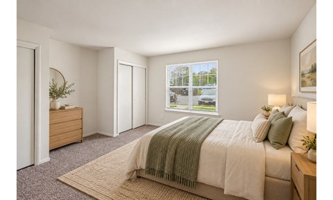 A bedroom with a bed, nightstand, and window overlooking a parking lot.