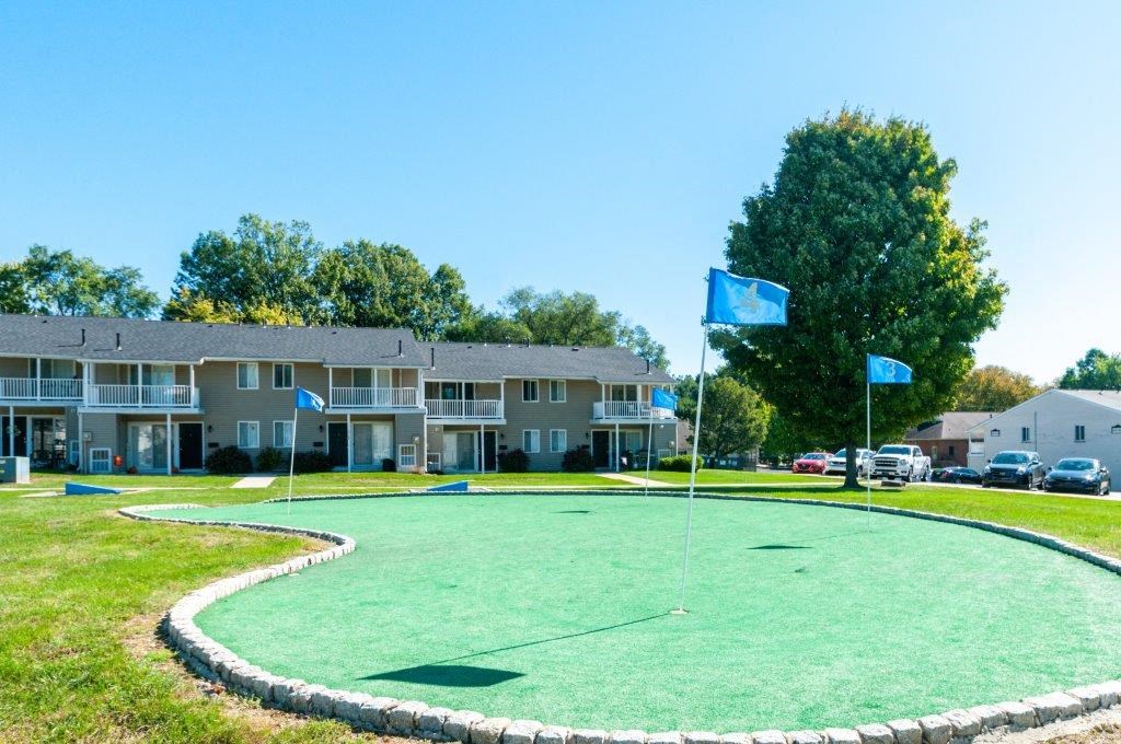 a putting green with blue flags in front of an apartment building