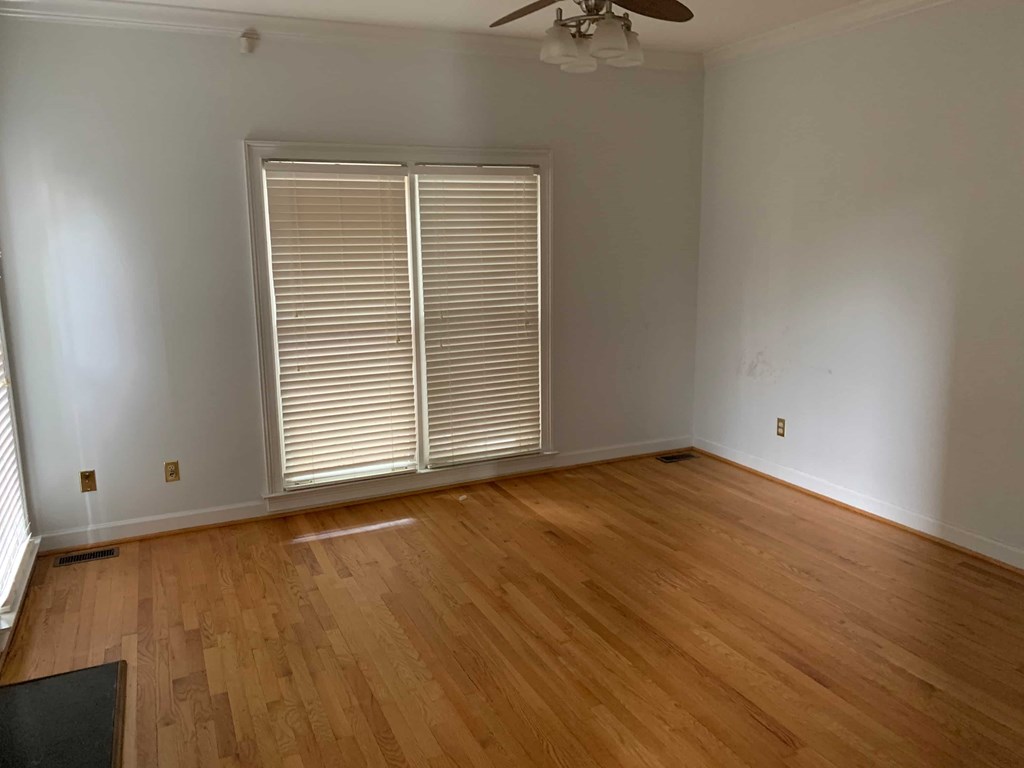 a living room with wooden floors and a large window with blinds