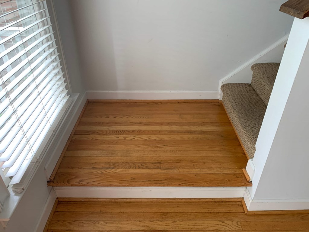 a stairway with wooden steps up to a window with blinds
