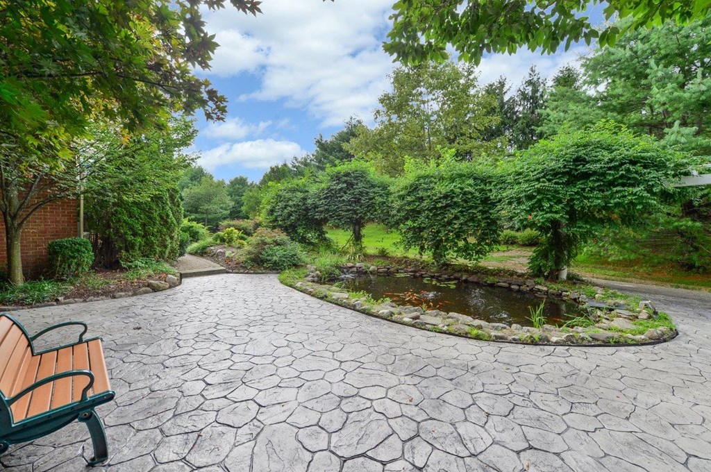 a walkway with a bench and a pond in a park