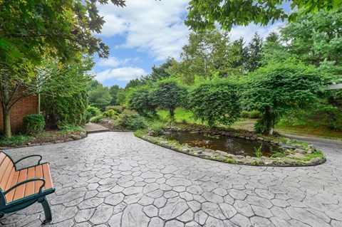 a walkway with a bench and a pond in a park