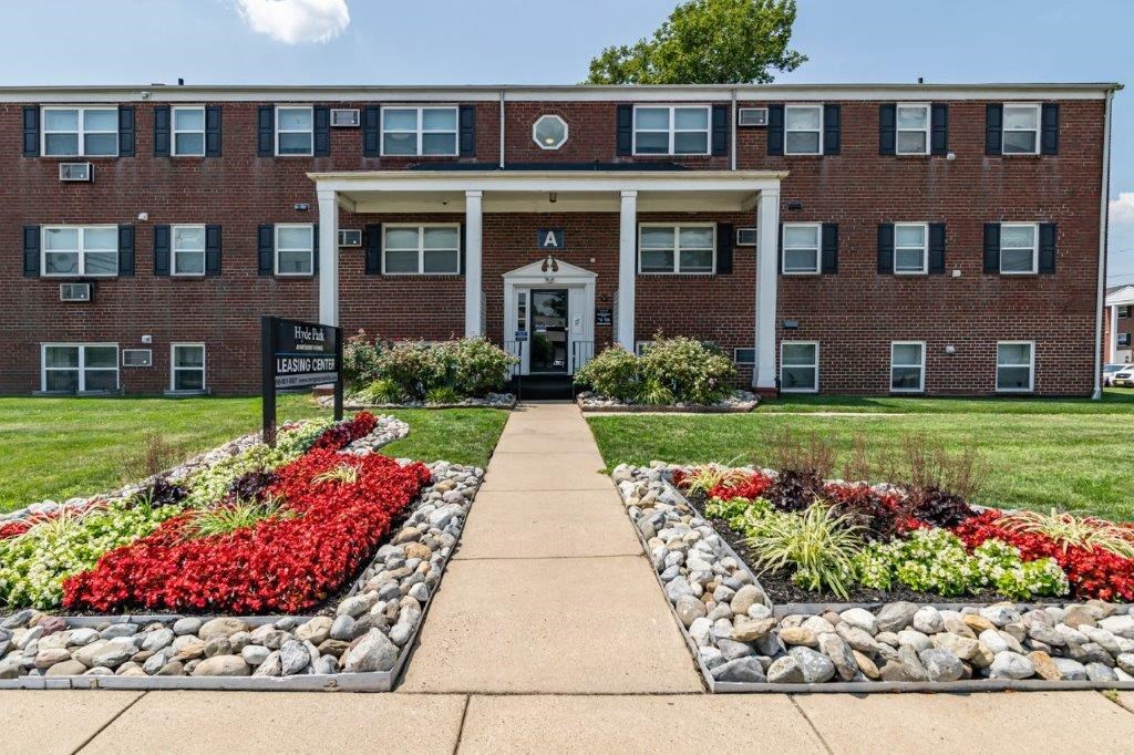 the front of a brick building with a sidewalk and rock garden