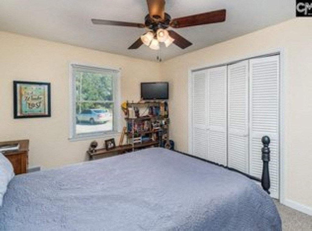 A bedroom with a bed, a ceiling fan, and a window with blinds.