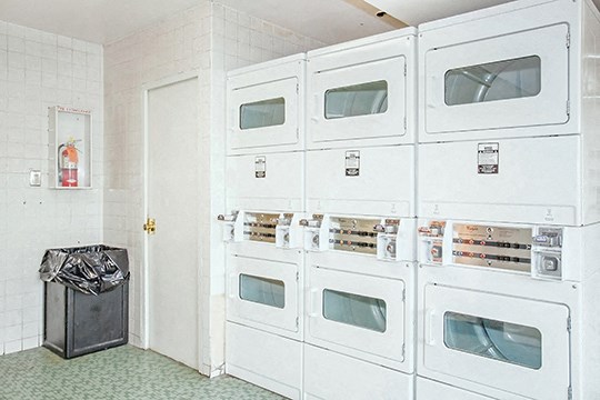 a row of white refrigerators in a room with a trash can