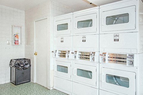 a row of white refrigerators in a room with a trash can