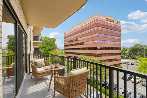 A balcony with a table and chairs overlooks a parking lot and a building.