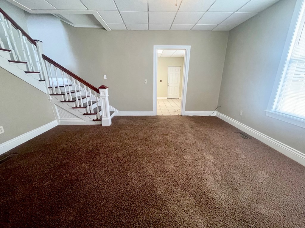 a carpeted living room with stairs and a door to a hallway