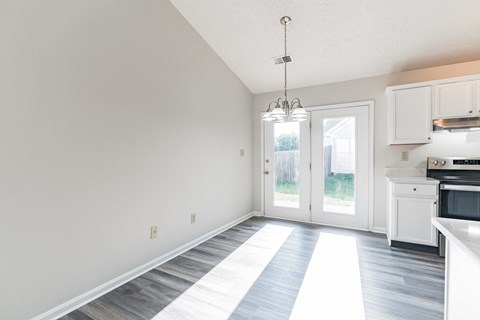 an empty living room and kitchen with white cabinets and a door to a backyard