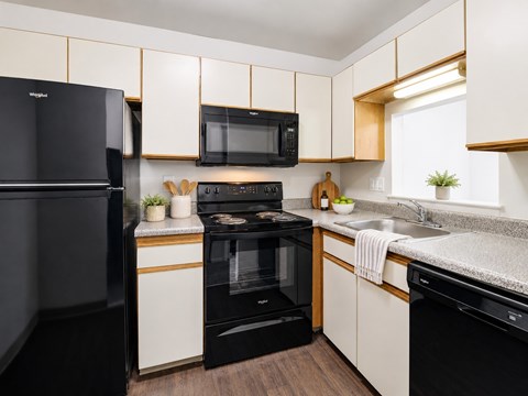 A black refrigerator is on the left in a kitchen with white cabinets.