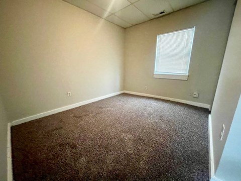 A room with a carpeted floor and a window with blinds.
