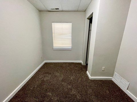 A room with a carpeted floor and a window with blinds.