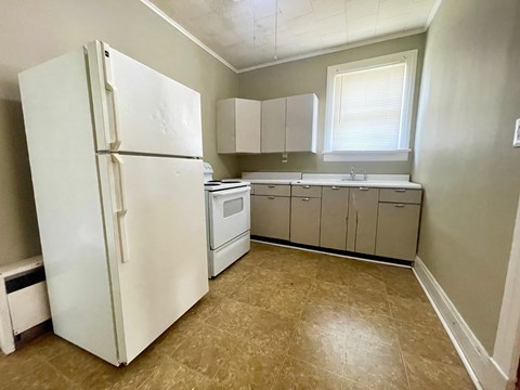 A white refrigerator is in a kitchen with beige cabinets and a tiled floor.