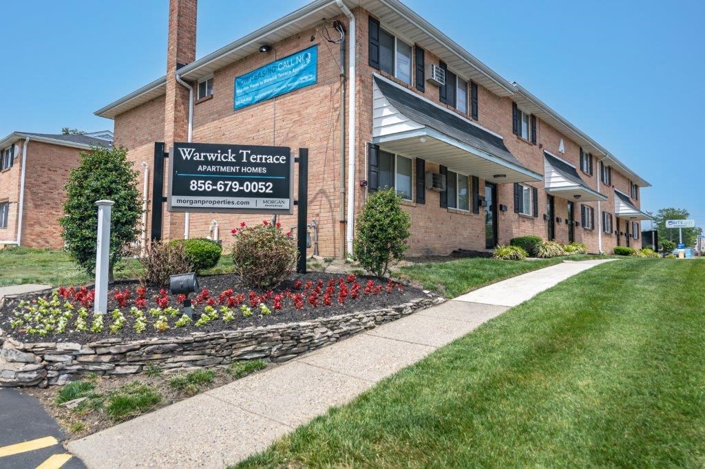 a brick building with a sidewalk and flower beds in front of it