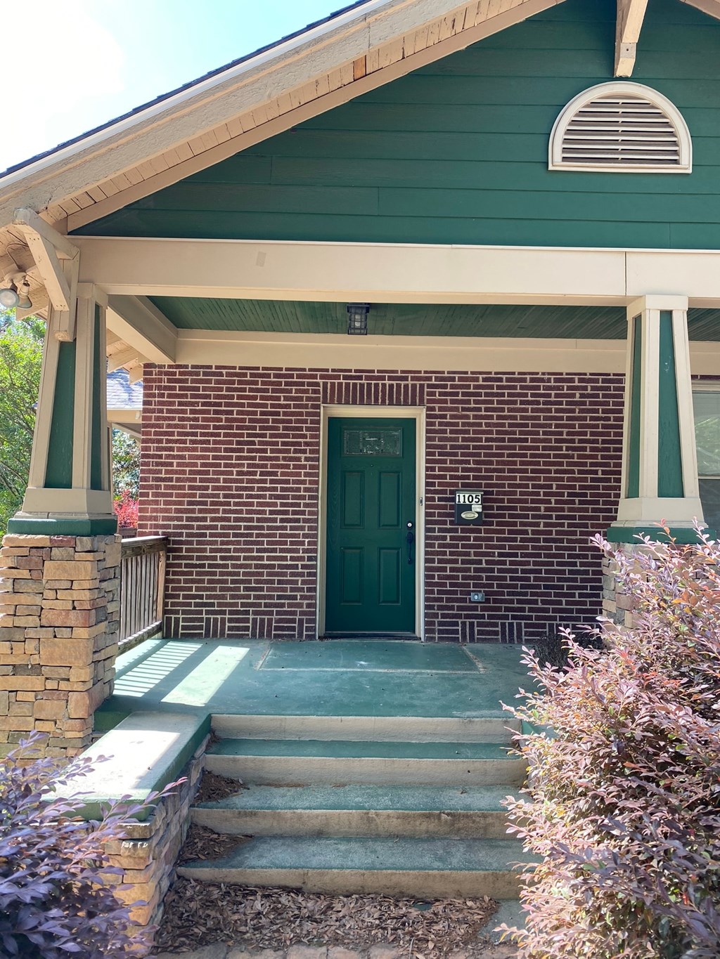 A green house with a green door and a brick wall.
