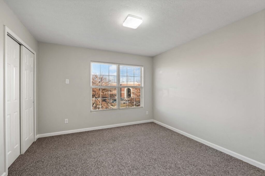 an empty bedroom with a large window and carpeting