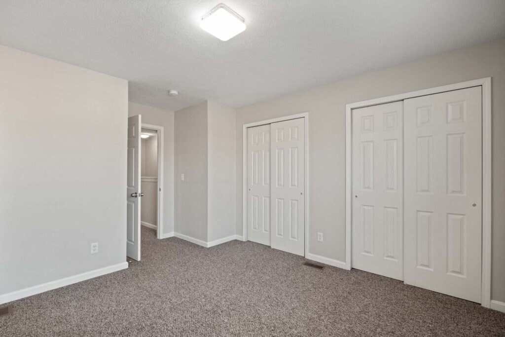 an empty bedroom with white doors and carpeted flooring