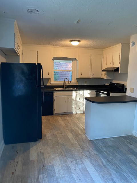 an empty kitchen with white cabinets and a black refrigerator