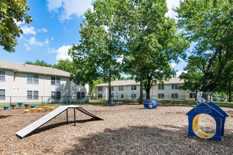 a playground in a park with trees and apartments in the background
