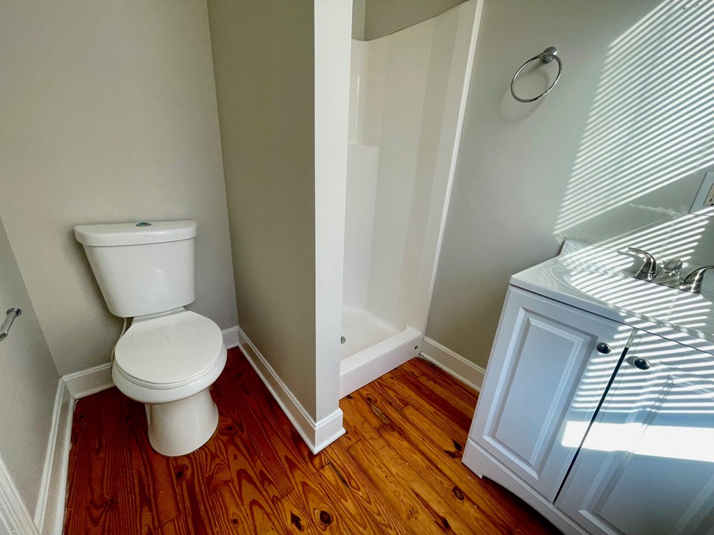 A white toilet sits in a bathroom with wood flooring.