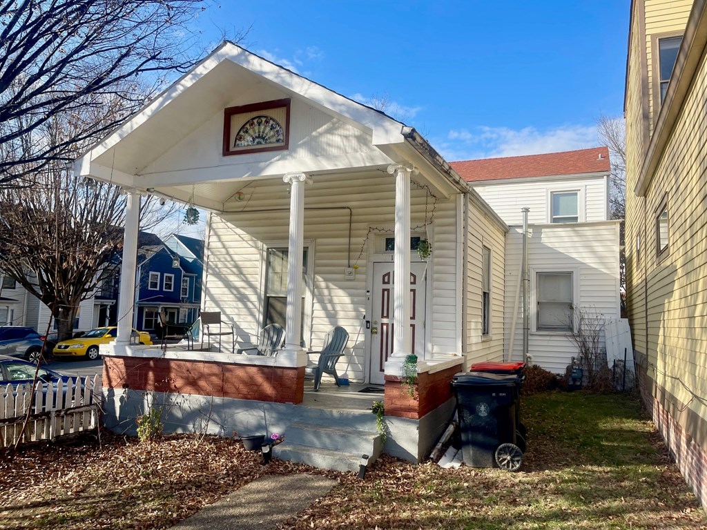 A small white house with a porch and a blue house in the background.