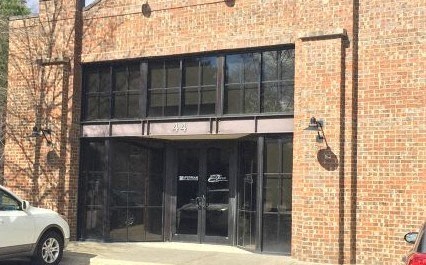 A white car is parked in front of a brick building with a black awning.