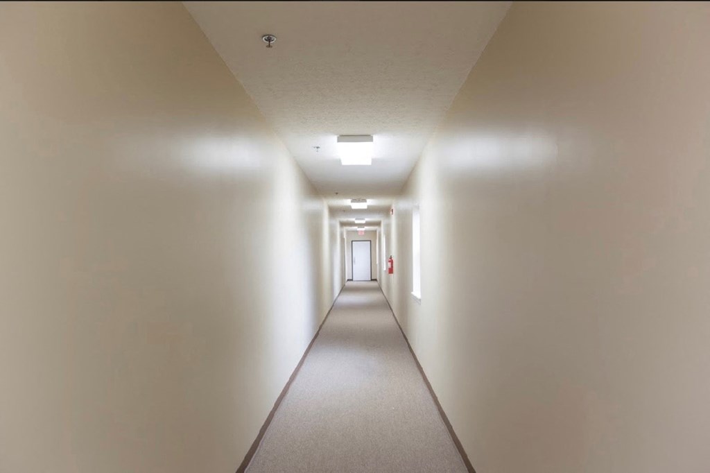 a long hallway with white walls and a red fire hydrant in the end