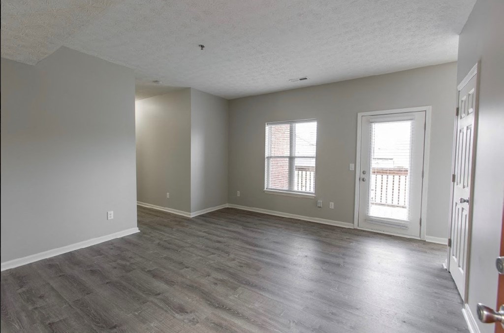 an empty living room with wood floors and a door to a balcony