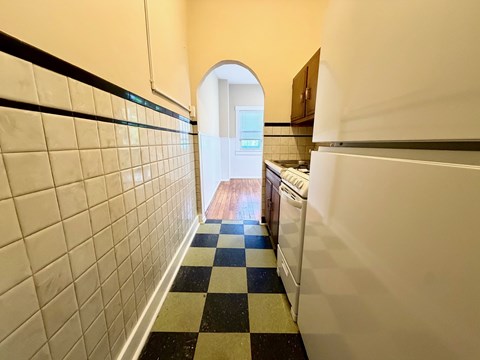 A hallway with a checkered floor leads to a kitchen.
