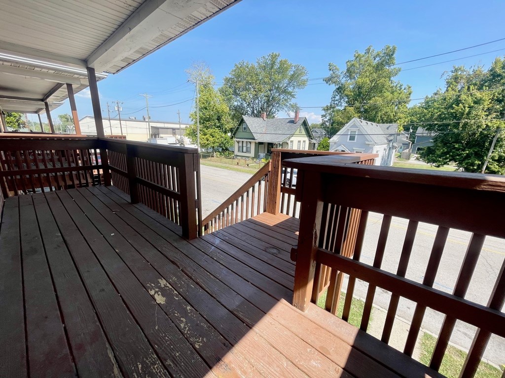 A wooden deck with a railing and a view of a street and houses.