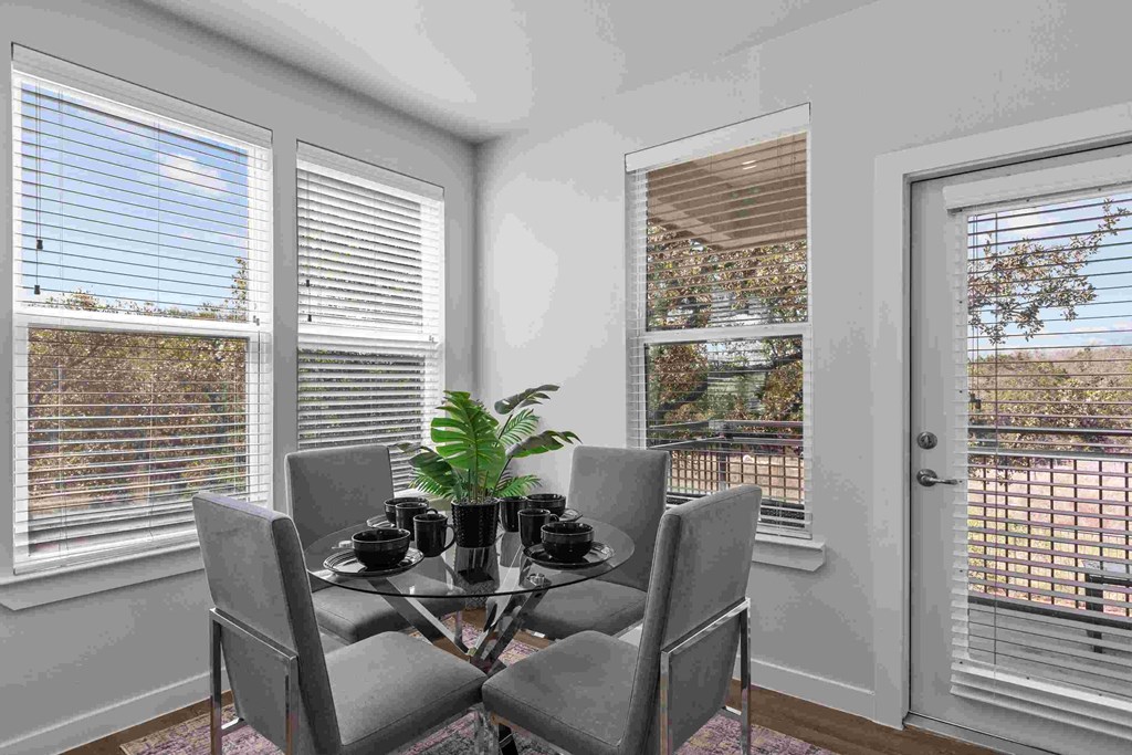 a dining room with a glass table and chairs and two windows