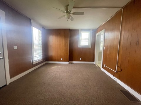 an empty living room with a ceiling fan and wood paneling