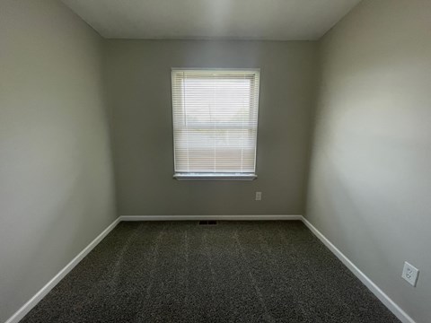 A room with a carpeted floor and a window with blinds.