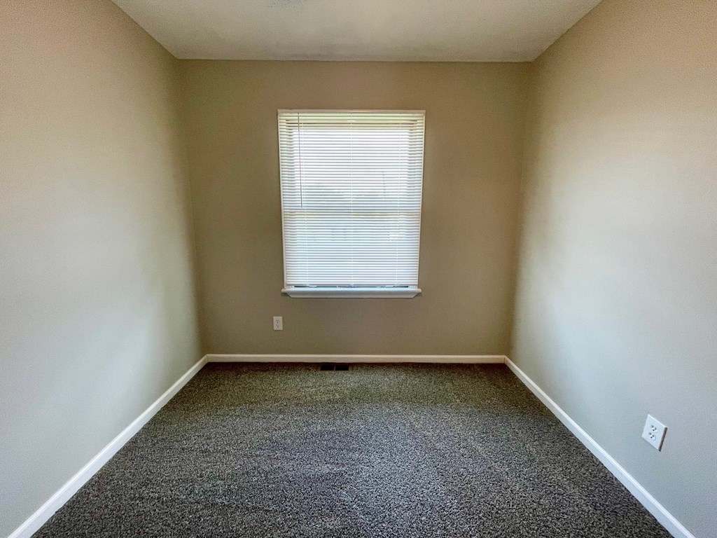 A room with a carpeted floor and a window with blinds.