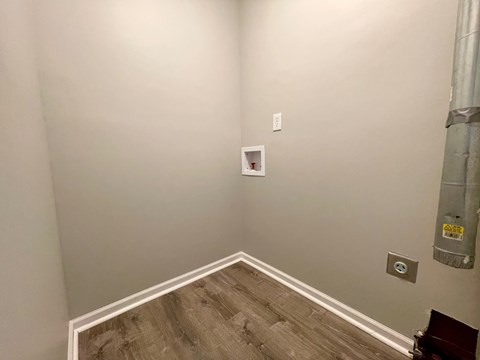 A room with a wooden floor and a white wall with a switch.
