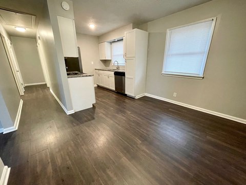 an empty living room with wood floors and a kitchen
