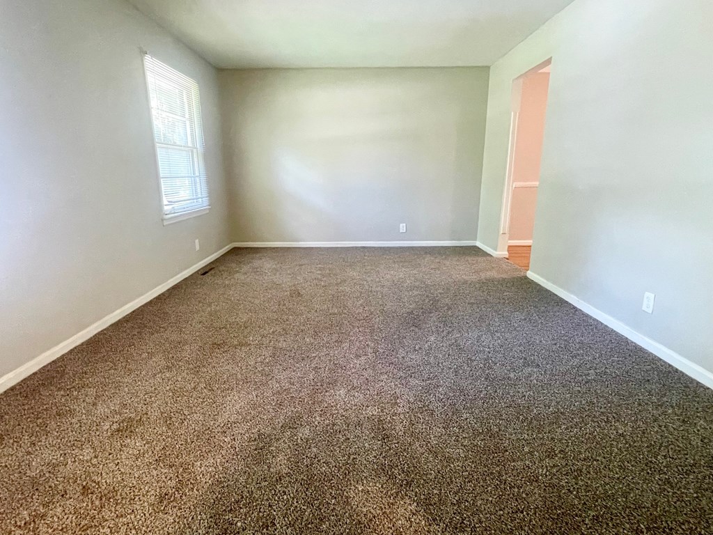 A room with carpeted floor and a window letting in sunlight.