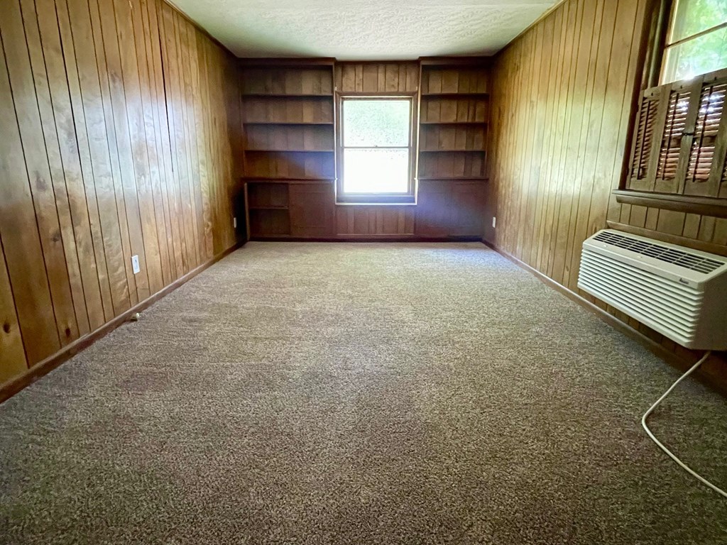 A room with wooden walls and a carpeted floor with a window and a heater.