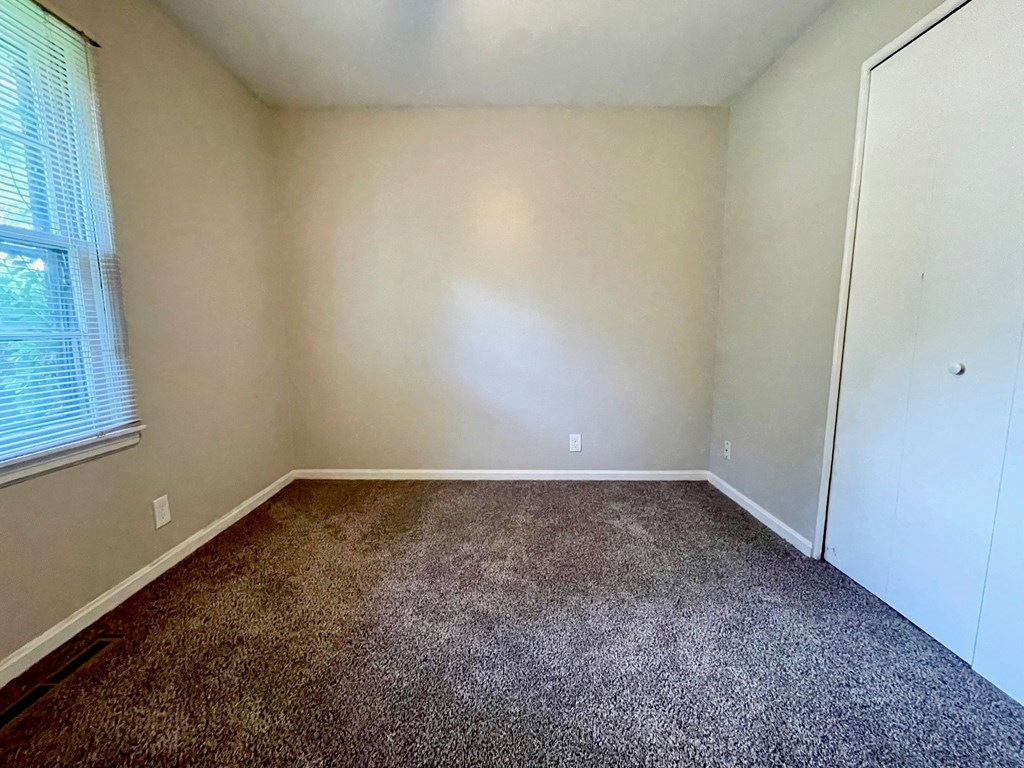A room with a carpeted floor and a window with blinds.