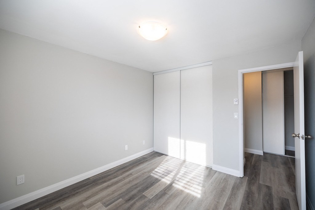 a bedroom with white walls and wood flooring and a closet