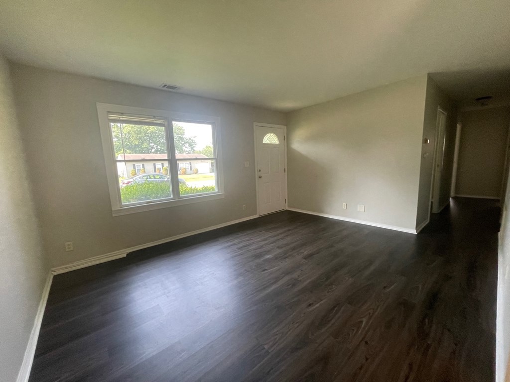 A room with wooden floors and a window showing a view of a building and trees.