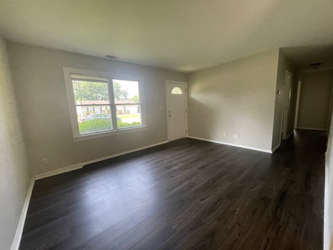 A room with wooden floors and a window showing a view of a building and trees.