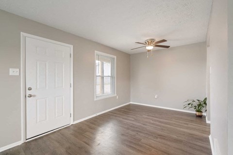 an empty living room with a white door and a ceiling fan